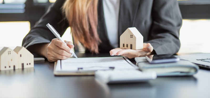 Real estate agent holding a wooden model house and making notes.