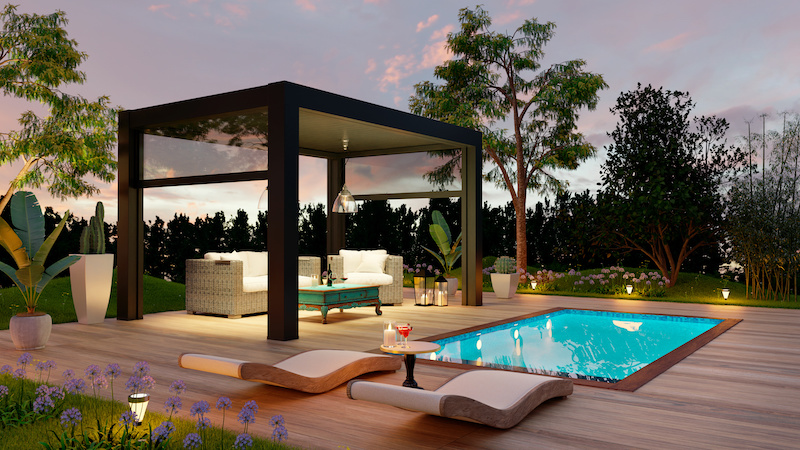 Luxury outdoor garden with wooden deck. Sofas and deck chairs next to the swimming pool at sunset.